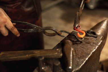 Erkek demircinin güçlü elleri yakın plan çalışmasında demircide demirden bir ürün dövüyor. Çekiç, sıcak metal ve örs. Çalışma anlayışı, geçmişe dönük meslekler