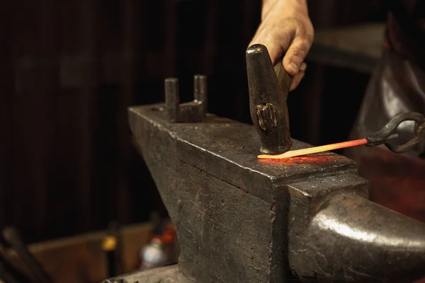 Egy közeli, dolgozó férfi kovács erős kezei kovácsolnak vasat egy kovácsban. Kalapács, vörös forró fém és üllő. A munka fogalma, retro szakmák — Stock Fotó
