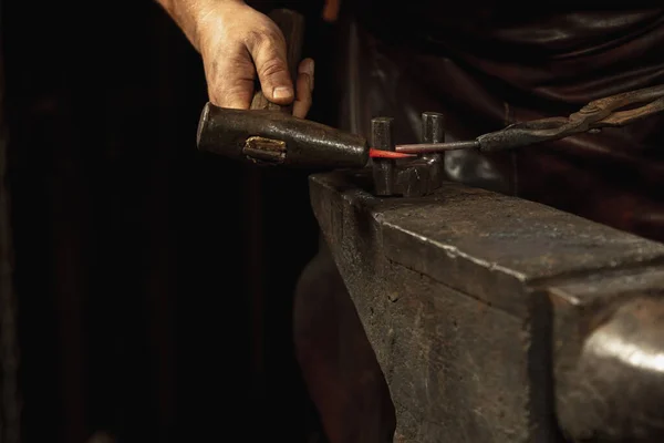 Mãos poderosas e fechadas do ferreiro forjam um produto de ferro num ferreiro. Martelo, metal quente vermelho e bigorna. Conceito de trabalho, profissões retro — Fotografia de Stock