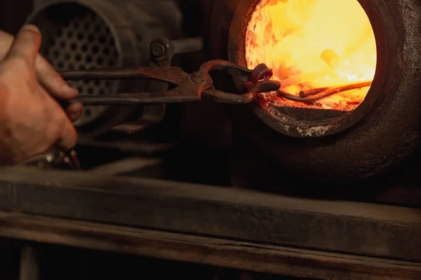Yakından çalışan erkek demircinin güçlü elleri fırında, boynuzda kırmızı sıcak metal yapıyor. Demircilikte metali ısıtma işlemi. Çalışma anlayışı, geçmişe dönük meslekler, aile meslekleri — Stok fotoğraf
