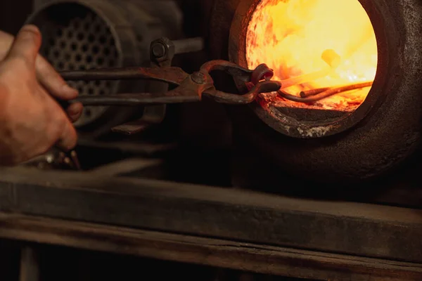 Primer plano trabajando poderosas manos de herrero macho haciendo metal caliente rojo en horno, cuerno. Proceso de trabajo de calentar metal en herrería. Concepto de trabajo, profesiones retro, empresa familiar —  Fotos de Stock