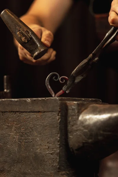 Egy közeli, dolgozó férfi kovács erős kezei kovácsolnak vasat egy kovácsban. Kalapács, vörös forró fém és üllő. A munka fogalma, retro szakmák — Stock Fotó