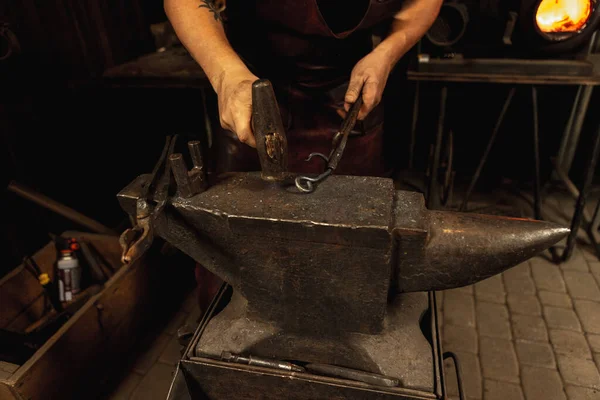 Mãos poderosas e fechadas do ferreiro forjam um produto de ferro num ferreiro. Martelo, metal quente vermelho e bigorna. Conceito de trabalho, profissões retro — Fotografia de Stock