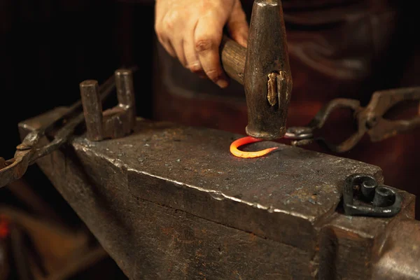 Mãos poderosas e fechadas do ferreiro forjam um produto de ferro num ferreiro. Martelo, metal quente vermelho e bigorna. Conceito de trabalho, profissões retro — Fotografia de Stock