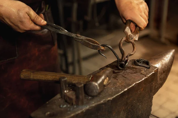 Mãos poderosas e fechadas do ferreiro forjam um produto de ferro num ferreiro. Martelo, metal quente vermelho e bigorna. Conceito de trabalho, profissões retro — Fotografia de Stock