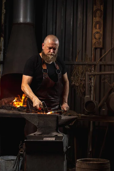 Homem barbudo, ferreiro que trabalha na criação de produtos metálicos artesanais em ferreiros familiares. Conceito de trabalho, profissões retro, poder, beleza — Fotografia de Stock