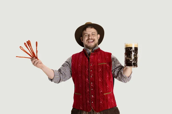 Close-up de homem barbudo, garçom em traje tradicional austríaco ou bávaro segurando caneca, vidro de cerveja preta escura isolada sobre fundo cinza — Fotografia de Stock