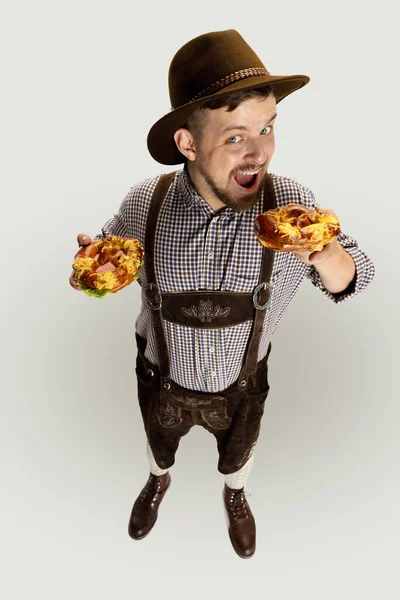 Blick aus der Vogelperspektive auf einen lächelnden Mann, Kellner in bayerischer Tracht mit leckeren Brezeln vor grauem Hintergrund. Nationale Küche, Feiertage, Traditionen — Stockfoto