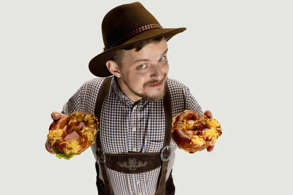 Vue grand angle de l'homme souriant, serveur en costume bavarois traditionnel avec bretzels délicieux isolés sur fond gris. Cuisine nationale, vacances, traditions — Photo