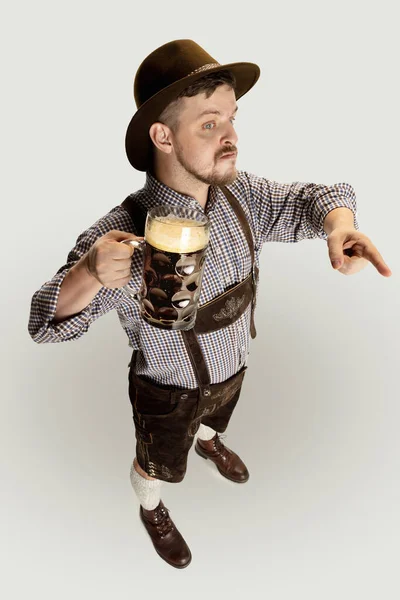 Vysoký úhel pohledu na vousatého muže, číšníka v tradičním rakouském nebo bavorském kostýmu držícího hrnek, sklo tmavého černého piva izolovaného na šedém pozadí — Stock fotografie