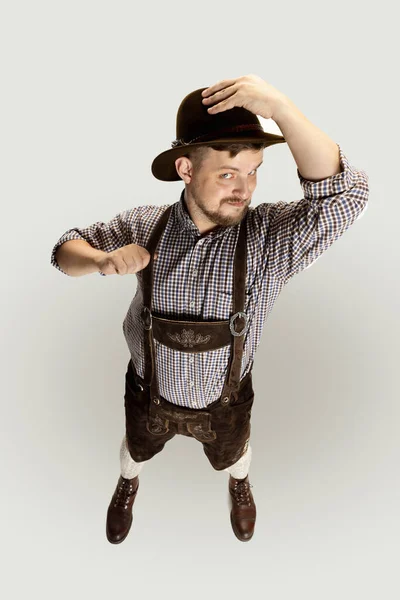 Гарний чоловік з бородою, офіціант в традиційному австрійському або баварському костюмі, який стоїть один ізольований над сірим фоном. Смішний мем. — стокове фото