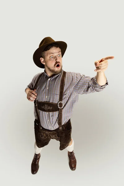 Słodki, zaskoczony brodaty mężczyzna, kelner w tradycyjnym austriackim lub bawarskim kostiumie stojący samotnie na szarym tle. Zabawne meme emocje — Zdjęcie stockowe