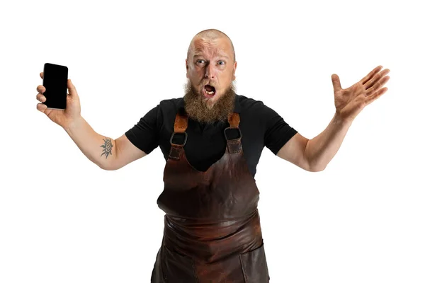 Comic portrait of muscular bearded bald man, blacksmith in leather apron or uniform isolated on white studio background. Concept of labor, retro professions, power, beauty, humor — Stock Photo, Image