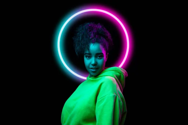 Retrato da menina sorridente feliz africana em luz de néon no fundo escuro estúdio com círculo azul neoned. Conceito de juventude, música, discoteca, anúncio, vendas — Fotografia de Stock