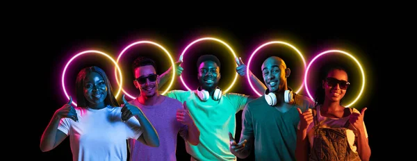 Colagem feita de jovens multiétnicos que estão juntos isolados no fundo do estúdio escuro em luz de néon multicolorida com forma luminescente geométrica circo — Fotografia de Stock
