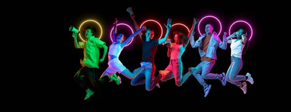 Koláž z multietnických mladých lidí skákání dohromady izolované na tmavém pozadí studia v pestrobarevném neonovém světle s geometrickým světélkujícím tvarem kruh — Stock fotografie
