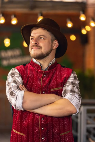 Caucasian bearded man, owner of restaurant in traditional Bavarian festive costume greeting customers, visitors at bar, cafe, pub. Oktoberfest — Stock Photo, Image