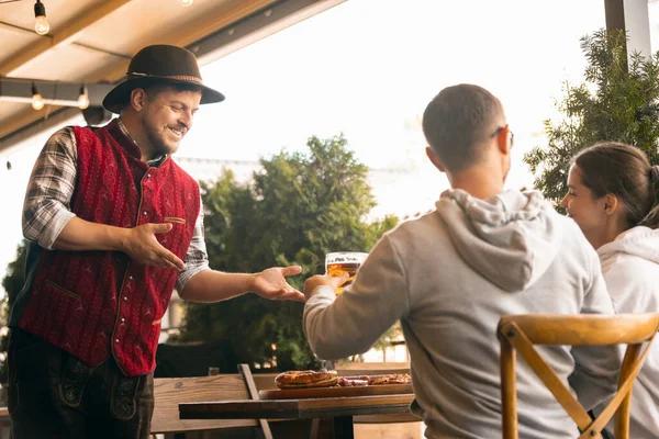 Grupo de amigos se reúnen en el bar, la cafetería y beber cerveza en el festival de la cerveza. Tradiciones, diversión, alegría, amistad, vacaciones. Festival de octubre, octubre, concepto de otoño — Foto de Stock