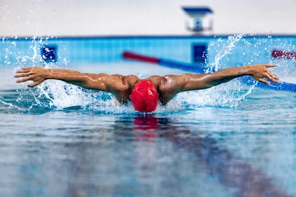 Nadador masculino profesional en gorra de natación y gafas en movimiento y acción durante el entrenamiento en la piscina, en interiores. Estilo de vida saludable, poder, energía, concepto de movimiento deportivo —  Fotos de Stock