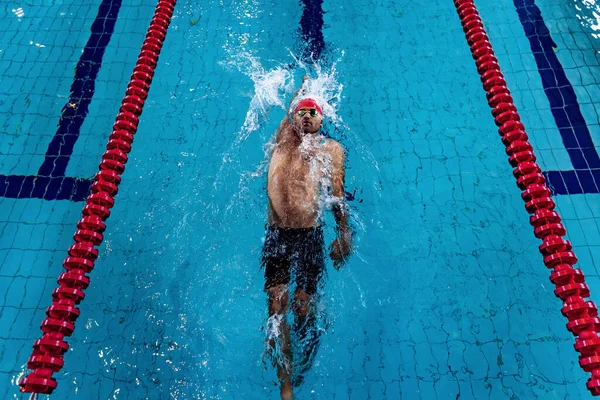 Молодой профессиональный пловец в красной кепке и очках практикуется и тренируется в бассейне, в помещении. Здоровый образ жизни, власть, энергия, концепция спортивного движения — стоковое фото