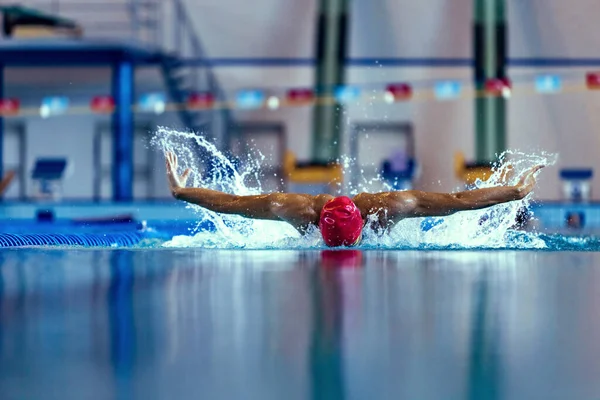 Nadador masculino profesional en gorra de natación y gafas en movimiento y acción durante el entrenamiento en la piscina, en interiores. Estilo de vida saludable, poder, energía, concepto de movimiento deportivo — Foto de Stock