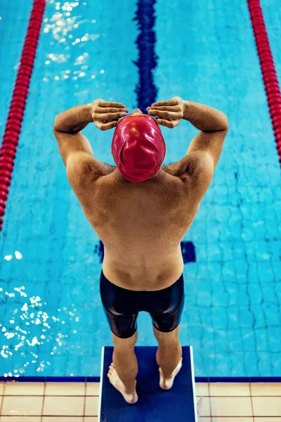 Al principio. Nadador masculino deportivo con gorra roja y gafas en movimiento y acción durante el entrenamiento en la piscina, en interiores. Estilo de vida saludable, poder, energía, concepto de movimiento deportivo —  Fotos de Stock