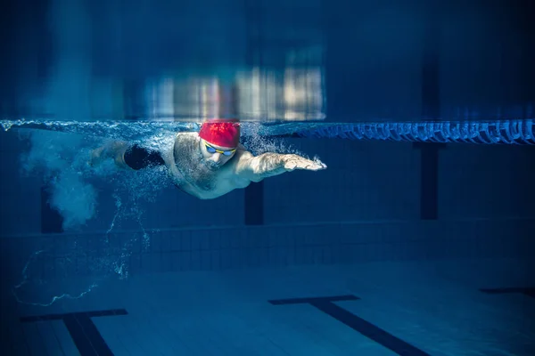 Um nadador do sexo masculino praticando e treinando na piscina, dentro de casa. Vista subaquática dos detalhes dos movimentos de natação. Estilo de vida saudável, poder, energia, conceito de movimento desportivo. — Fotografia de Stock