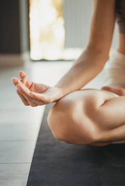 Cropped image of young slim sportive woman in sportswear doing yoga exercise on sports mat at yoga meditation center. Concept of healthy lifestyle, wellbeing, mental health