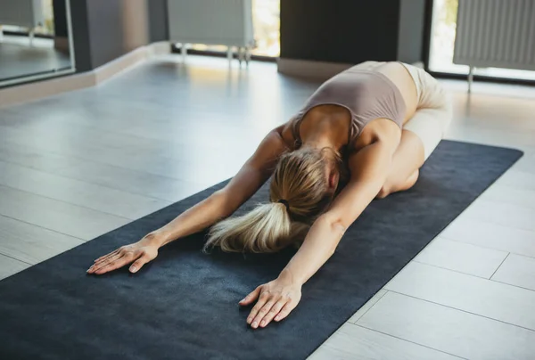 Clase de yoga. Retrato de una joven deportista en ropa deportiva haciendo ejercicio sobre alfombra deportiva en el centro de meditación de yoga. Concepto de estilo de vida saludable, bienestar, salud mental — Foto de Stock