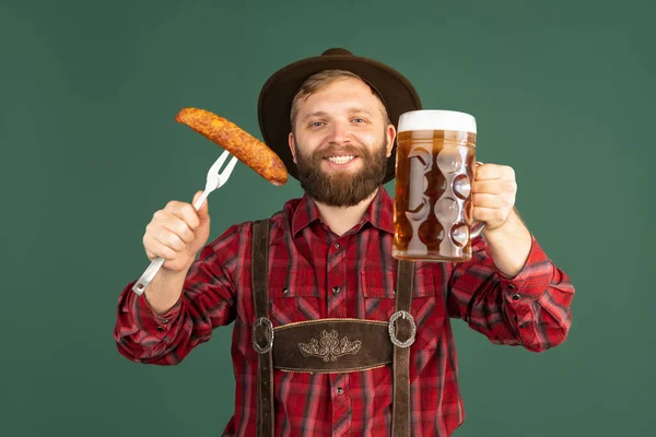 Retrato de hombre barbudo, camarero en traje bávaro tradicional con un litro de cerveza oscura aislada sobre fondo verde. Oktoberfest, festival, concepto de tradiciones —  Fotos de Stock