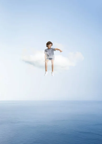 Kreatív kollázs kis óvodás fiúval, aki fehér felhőn ül és az égen repül, a szabadban. Fogalom gyermekkor, boldogság, álmok, kaland — Stock Fotó