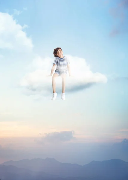 Colagem criativa com pequeno menino pré-escolar sentado na nuvem branca e voando no céu, ao ar livre. Conceito de infância, felicidade, sonhos, aventura — Fotografia de Stock