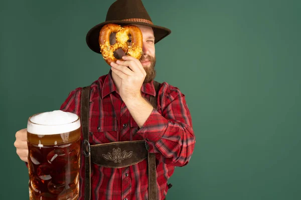 Retrato de hombre barbudo, camarero en traje bávaro tradicional con un litro de cerveza oscura aislada sobre fondo verde. Oktoberfest, festival, concepto de tradiciones —  Fotos de Stock