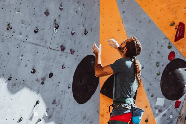 Jeune homme grimpeur professionnel assiste quelqu'un sur le mur d'escalade au centre d'entraînement par temps ensoleillé, en plein air. Concept de force, mouvement. — Photo