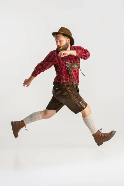 Fullängds porträtt av skäggig man i hatt och traditionella bayerska kostym kör iväg isolerad över vit bakgrund. Flyer, oktoberfest koncept — Stockfoto