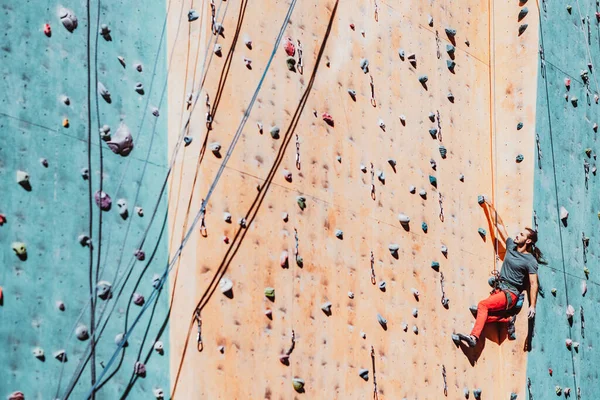 Um homem caucasiano desportista profissional, treinos de alpinista na parede de escalada no centro de treinamento em dia ensolarado, ao ar livre. Conceito de força, movimento. — Fotografia de Stock