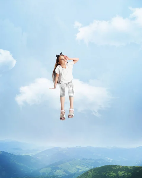Creative artwork, collage with little beautiful girl sitting on white cloud and flying above forest, nature landscape. Concept of childhood, happiness, dreams