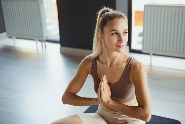 Retrato de jovem menina feliz esportiva, treinador em sportswear fazendo meditação de ioga no tapete esportivo no centro de meditação, dentro de casa. Conceito de estilo de vida saudável — Fotografia de Stock