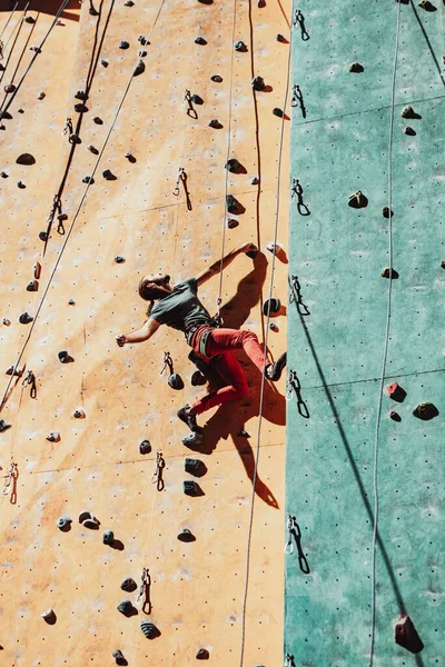 Un hombre caucásico entrenamientos profesionales escalador de roca en la pared de escalada en el centro de entrenamiento en el día soleado, al aire libre. Concepto de estilo de vida saludable, poder, fuerza, movimiento. — Foto de Stock