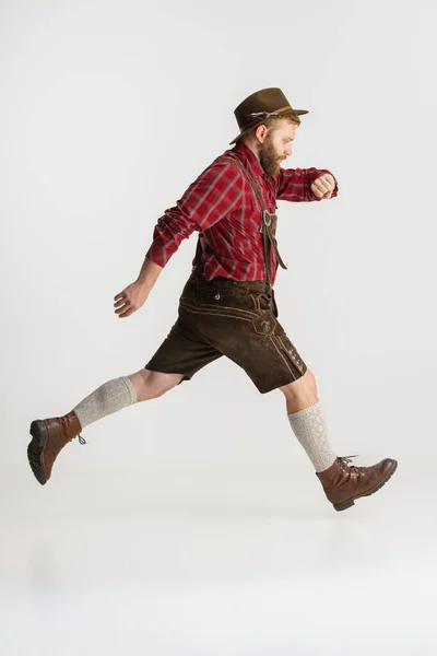 Full-length portrait of bearded man in hat and traditional Bavarian costume running away isolated over white background. Flyer, oktoberfest concept — Stock Photo, Image