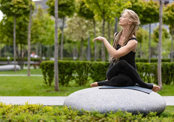 Mulher bonita nova com cabelo loiro fazendo exercício de ioga no parque público verde na manhã de verão, ao ar livre. Estilo de vida saudável, conceito de saúde mental. — Fotografia de Stock