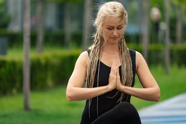Close-up tiro de mulher bonita com cabelo loiro fazendo exercício de ioga no parque público verde na manhã de verão, ao ar livre. Estilo de vida saudável, conceito de saúde mental. — Fotografia de Stock
