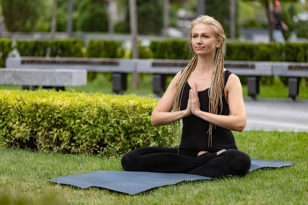 Sarı saçlı genç bir kadın yaz sabahı yeşil halk parkında yoga yapıyor. Açık havada. Sağlıklı yaşam tarzı, zihinsel sağlık konsepti. — Stok fotoğraf