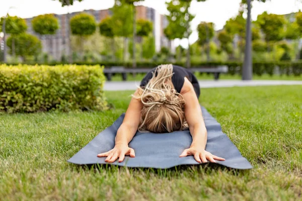 Junge schöne Frau mit blonden Haaren macht Yoga-Übungen im grünen öffentlichen Park im Sommer morgens, im Freien. Gesunder Lebensstil, Konzept für psychische Gesundheit. — Stockfoto