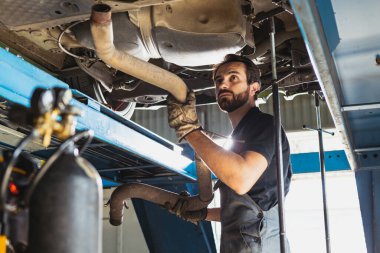 Genç bir adamın portresi, kapalı bir yerde, araba servis istasyonunda çalışan, tulumlu erkek oto tamircisi. Çalışma kavramı, meslek, iş, kariyer, iş