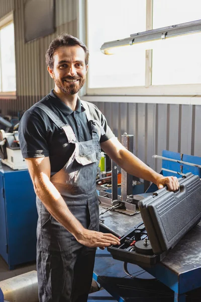 Joven hombre caucásico, mecánico de automóviles en dungarees trabajando en la estación de servicio de automóviles, en interiores. Concepto de trabajo, ocupación, negocio, caree, trabajo —  Fotos de Stock