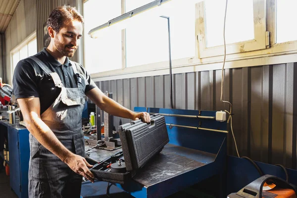 Preparándose para la reparación. Un hombre joven, mecánico de automóviles en Dungarees trabajando en la estación de servicio de automóviles, en interiores. Concepto de trabajo, ocupación, negocio, caree, trabajo —  Fotos de Stock