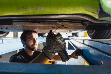 Genç bir adamın yakın çekimi, tulumlu erkek araba tamircisi araba servisi yapıyor istasyon, garaj, kapalı mekanda. Çalışma kavramı, meslek, iş, kariyer, iş