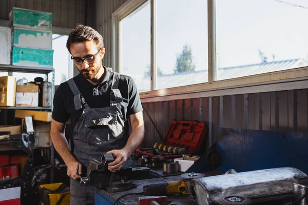 En la estación de servicio. Un hombre joven, mecánico de automóviles en Dungarees trabajando en la estación de servicio de automóviles, en interiores. Concepto de trabajo, ocupación, negocio, caree, trabajo —  Fotos de Stock