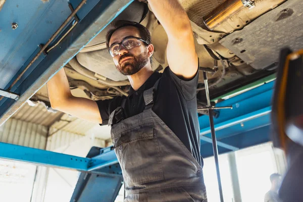 Πορτρέτο του νέου άνδρα, αρσενικό auto μηχανικός σε dungarees που εργάζονται σε σταθμό εξυπηρέτησης αυτοκινήτων, σε εσωτερικούς χώρους. Έννοια της εργασίας, επάγγελμα, επιχείρηση, καριέρα, εργασία — Φωτογραφία Αρχείου